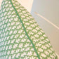 Close-up of the Burma Meadow Outdoor Pillow—green with a white leaf pattern and green piping—crafted from premium materials, shown against a light grey background.
