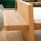 The Euclid Daybed, with its expertly crafted wooden armrest and intricately woven rope detail, sits elegantly on a beige textured carpet. Close by, a green chair and a stack of books, featuring one titled "ROLEX," enhance the scene's charm—a perfect blend of elegance and style reminiscent of the daybed itself.