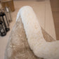 A fluffy white blanket draped over the arm of a patterned beige chair with lanterns displayed in the background, showcasing special attention to detail and custom-made Foliage Mushroom Pillow.