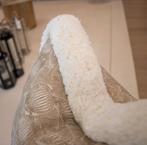 A fluffy white blanket draped over the arm of a patterned beige chair with lanterns displayed in the background, showcasing special attention to detail and custom-made Foliage Mushroom Pillow.