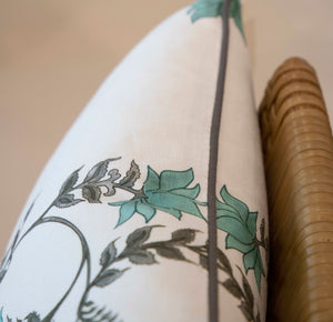 Close-up of a Poppy Stripe Aqua Lumbar Pillow with a floral design featuring green and gray leaves, draped over a wicker object, showcasing the finest materials with meticulous attention to detail.