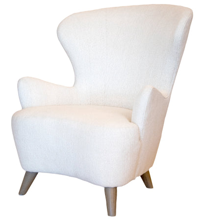 The Ollie Chair is a white, modern, high-back armchair with wooden legs, combining easy style with the timeless elegance of a classic wing chair.