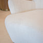 Close-up of a modern, textured white Ollie Chair with wooden legs, exuding comfort and easy style against a light-colored background.