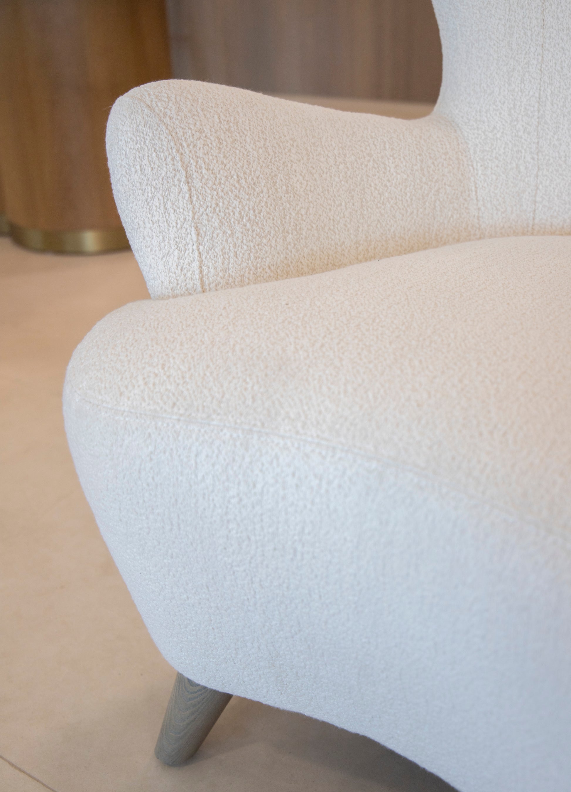 Close-up of a modern, textured white Ollie Chair with wooden legs, exuding comfort and easy style against a light-colored background.