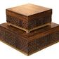 Two square, wooden boxes from the Oti Brown Box Collection with carved symbols and geometric patterns on their sides are stacked on top of each other. Crafted from mango wood, the surface of the boxes is smooth and polished.