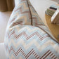 A close-up of the Ziggy Sky Pillow, a custom-made decorative piece featuring a blue, beige, and brown zigzag pattern on a light surface indoors.