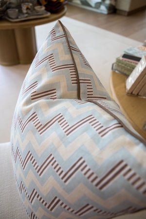 A close-up of the Ziggy Sky Pillow, a custom-made decorative piece featuring a blue, beige, and brown zigzag pattern on a light surface indoors.