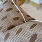 Close-up of the Abacus Walnut Reverse Pillow, a brown decorative pillow with white dotted and oval patterns and white piping along the edge—highlighting custom-made quality.