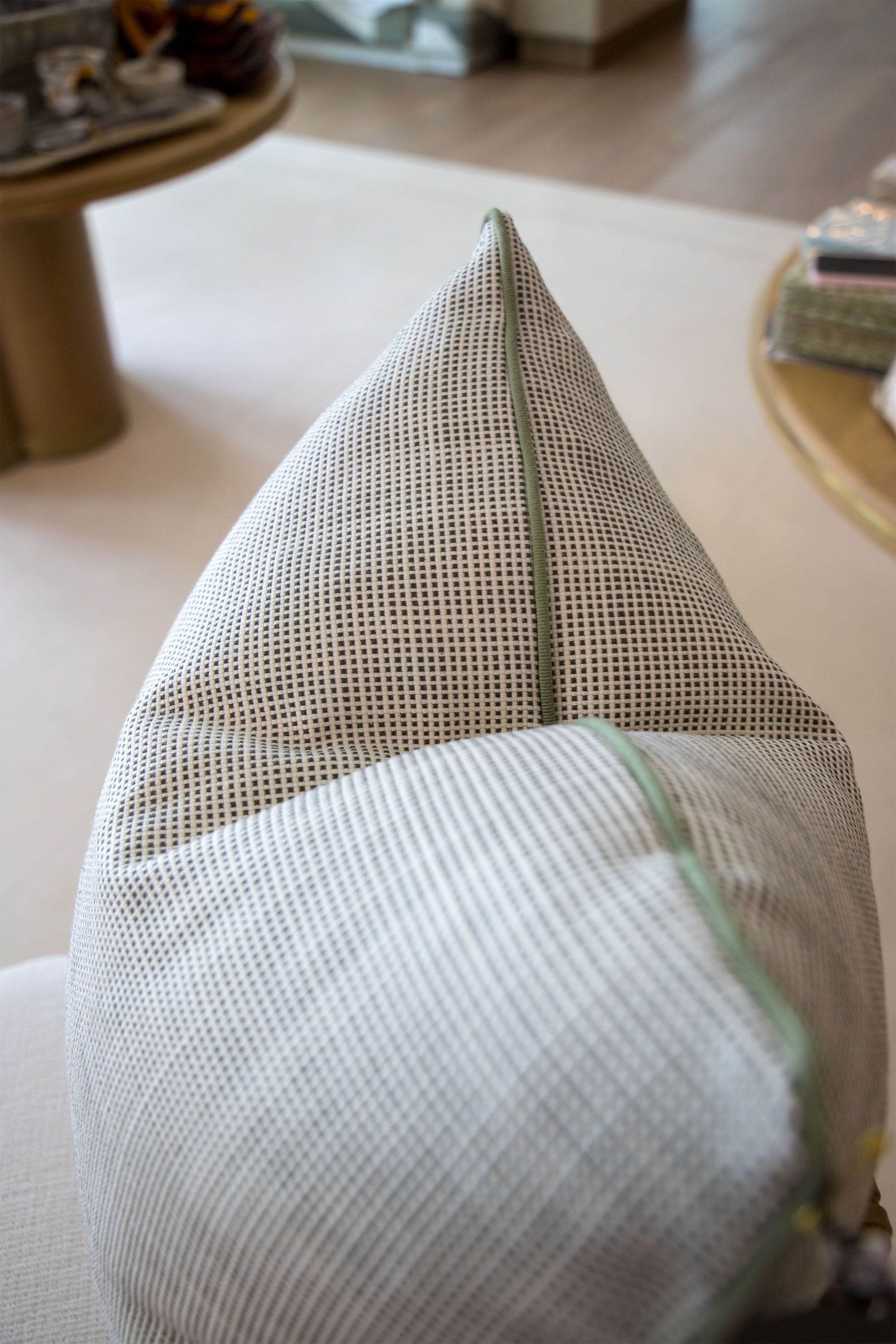 A close-up of the Helios Olive Pillow, a gray and white textured custom-made pillow with a green zipper, crafted from premium materials and displayed on a light-colored surface indoors.