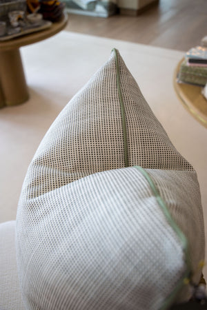 A close-up of the Helios Olive Pillow, a gray and white textured custom-made pillow with a green zipper, crafted from premium materials and displayed on a light-colored surface indoors.