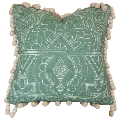 The Medinas Spruce Pillow is a square green decorative pillow, custom-made with premium materials, showcasing a white geometric and floral pattern and beige pom-pom trim along the edges.