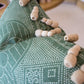The Medinas Spruce Pillow is a green patterned, custom-made pillow featuring several tan, finger-like objects resting on top.
