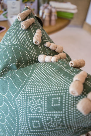 The Medinas Spruce Pillow is a green patterned, custom-made pillow featuring several tan, finger-like objects resting on top.