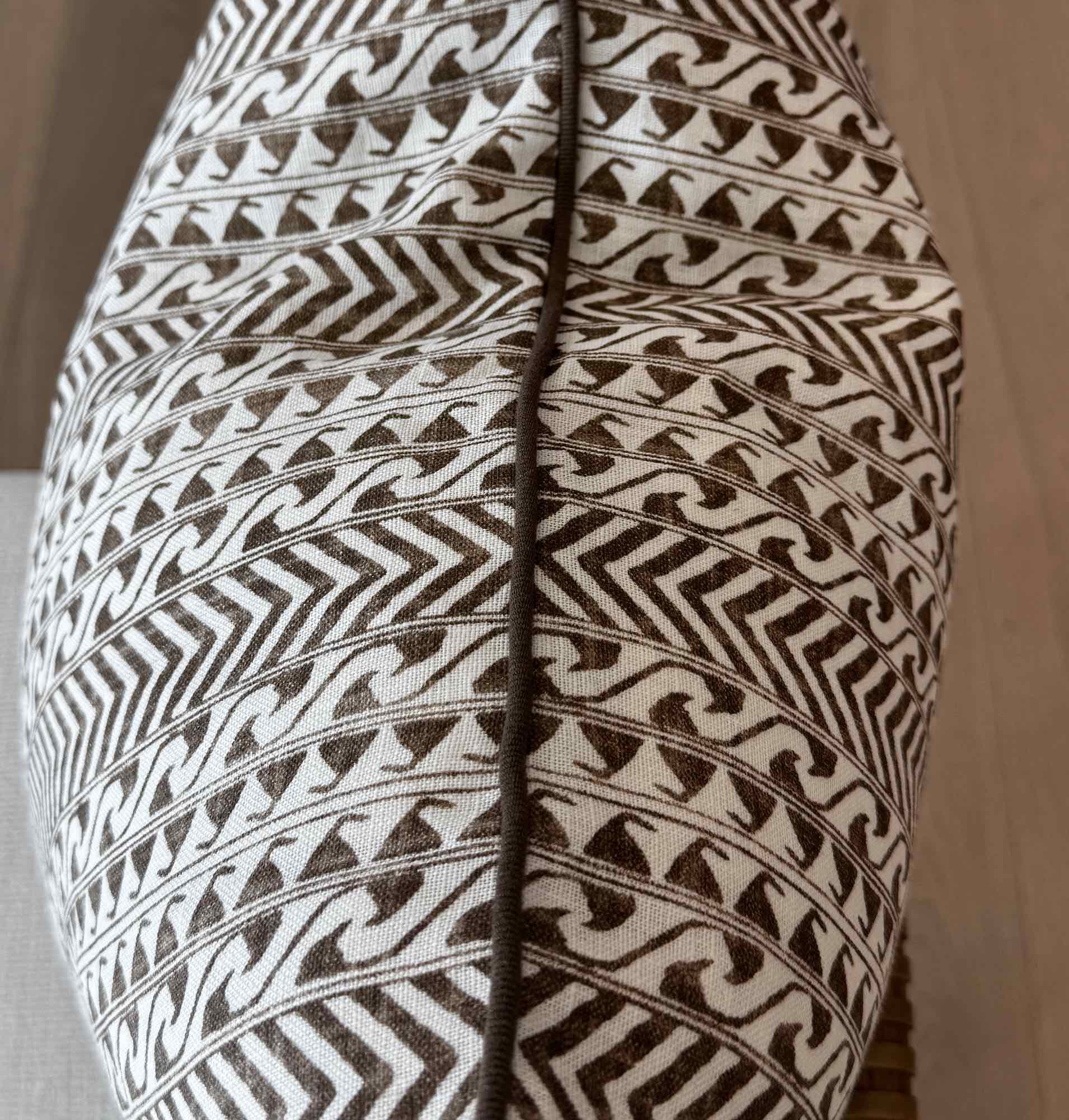 Close-up of the Luxor Coco Oyster Pillow’s fabric, featuring brown geometric and bird-like patterns divided by a vertical seam—ideal for custom-made pillows crafted from premium materials.