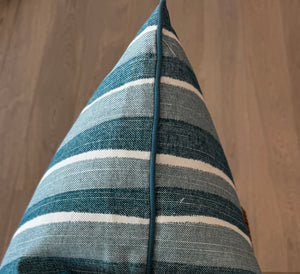 Close-up of the Orchard Stripe Pillow, a blue and white striped cushion with a pointed edge, crafted from premium materials and placed on a light wooden floor.