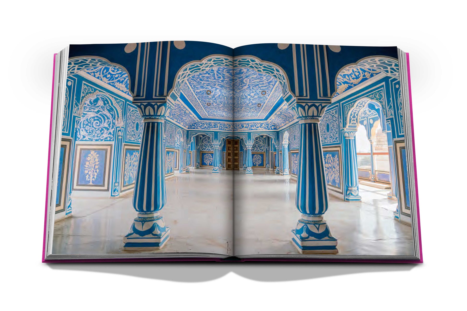 A hardcover book open to a photograph of an ornate, blue and white room with intricately detailed arches, columns, and ceiling designs, reminiscent of the Jaipur Splendor.