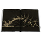 An open copy of "The Last Heroes: 100 MOMENTS OF OLYMPICS LEGEND" displays a sequence of photographs depicting a man with a rifle captured mid-jump against a dark background, echoing the energy of the Summer Olympics.
