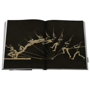 An open copy of "The Last Heroes: 100 MOMENTS OF OLYMPICS LEGEND" displays a sequence of photographs depicting a man with a rifle captured mid-jump against a dark background, echoing the energy of the Summer Olympics.