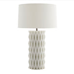 The Nago Lamp features a textured, geometric ceramic base inspired by modern Parisian architecture and is topped with a linen drum shade.