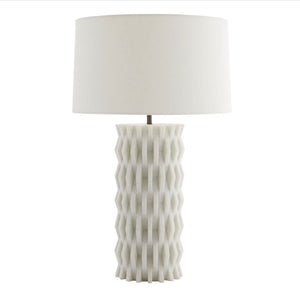 The Nago Lamp features a textured, geometric ceramic base inspired by modern Parisian architecture and is topped with a linen drum shade.