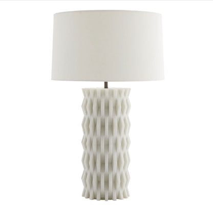 The Nago Lamp features a textured, geometric ceramic base inspired by modern Parisian architecture and is topped with a linen drum shade.