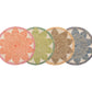 Four round placemats from the Kim Seybert Majorelle Placemat Collection are arranged side by side, displaying geometric patterns in pink, green, tan, and blue hues inspired by seagrass and subtle floral motifs.