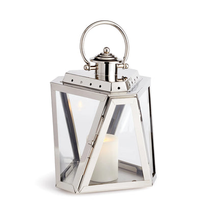 The Napa Adler Steel Outdoor Lantern features a silver metal and glass design with a chrome finish, a top handle, and includes a white LightLi pillar candle inside.