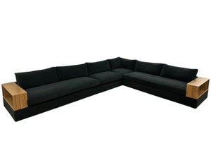 The Embrace Sectional in Vacation Charcoal offers spacious seating and built-in light wood side tables at each end for a modern touch. This large, black L-shaped sofa is shown against a white background.