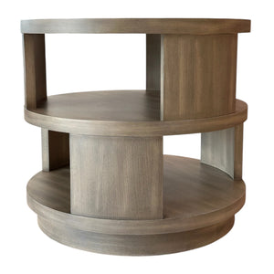 The Middleton End Table in Foundry is a round wooden table with two shelves and vertical supports, showcasing a light brown finish and minimalist design—ideal as an accent piece for modern spaces.