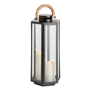 The Dockside Lantern in Black features stainless steel and glass construction, a teak handle, and holds two glowing white pillar candles inside.