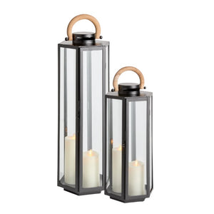 Two Dockside Lanterns in Black, hexagonal metal frames with glass panels and teak handles, each holding a white pillar candle.