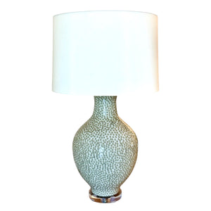 The Athens Large Green Dappled Lamp features a round, textured ceramic base with a dotted pattern and a large white cylindrical lampshade, beautifully photographed against a white background.