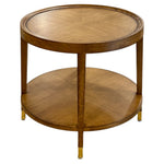 The Savoy Side Table, Wheat features a round wooden frame in a wheat finish, a lower shelf, and brass-capped feet for a simple, elegant look.
