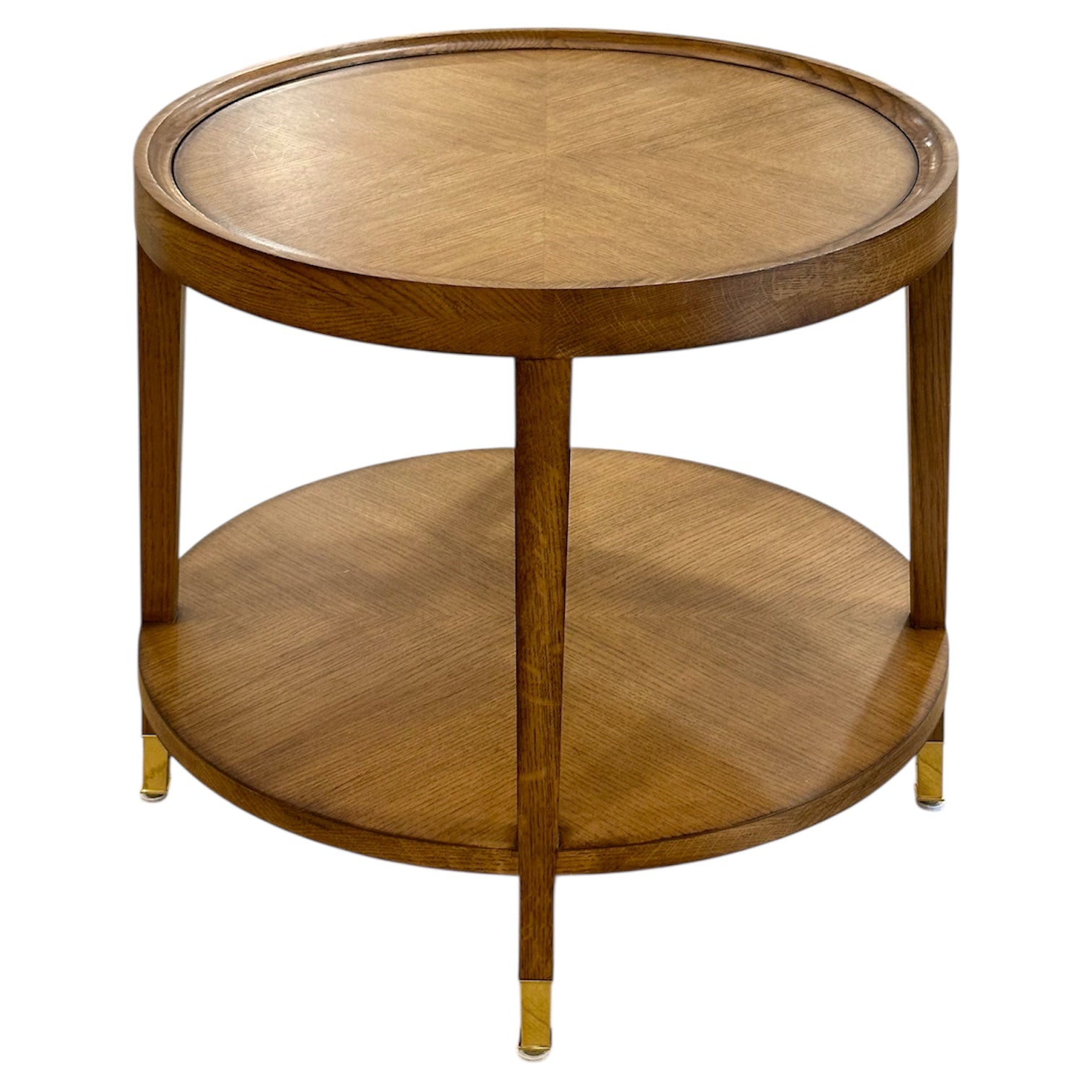 The Savoy Side Table, Wheat features a round wooden frame in a wheat finish, a lower shelf, and brass-capped feet for a simple, elegant look.