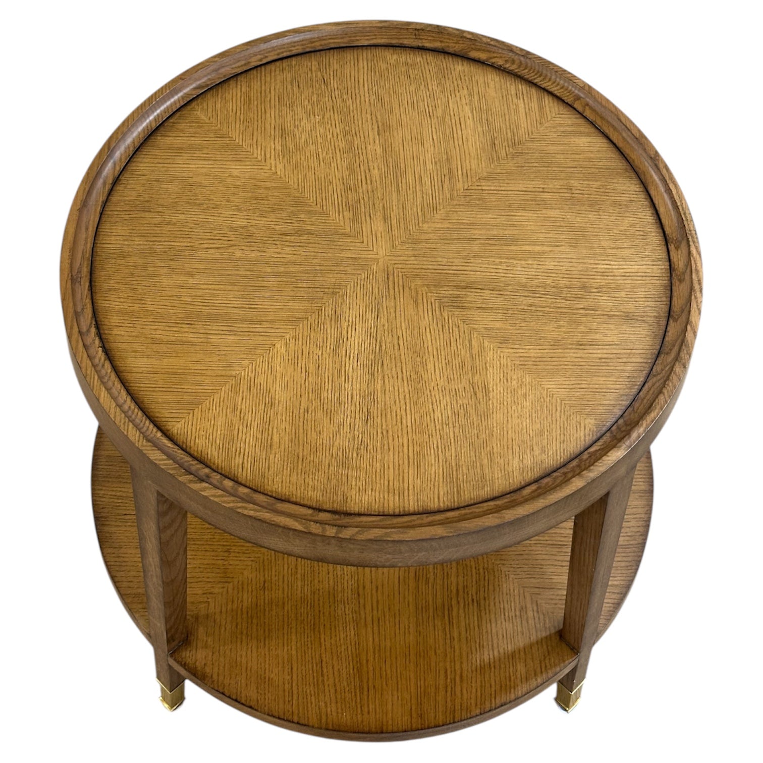 The Savoy Side Table, Wheat, is a round wooden table with an elegant design, showcasing a wood grain pattern on its top surface, lower shelf, and four legs as seen from above.