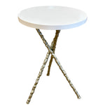 The Diego Side Table features a small round white resin top supported by three twisted iron legs in an intersecting minimalist design.