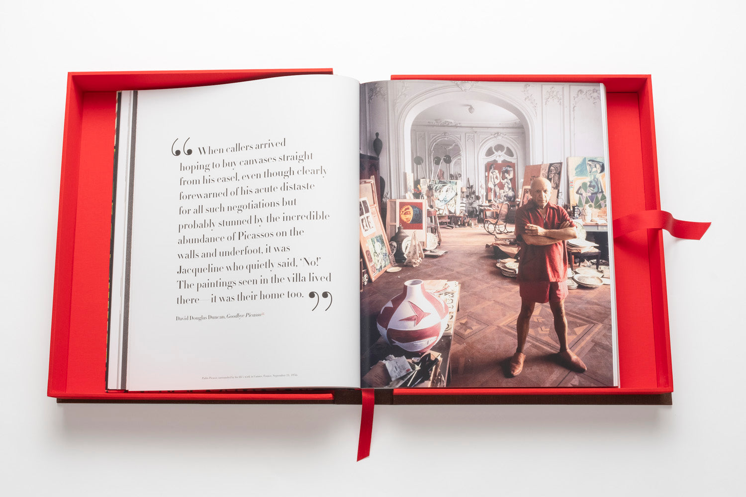 An open book in a red box displays a quote on the left page and a photo of a room with a standing person on the right. The room is filled with various art pieces and decorations, all reminiscent of twentieth-century influential artists, as seen in "The Impossible Collection: Picasso.