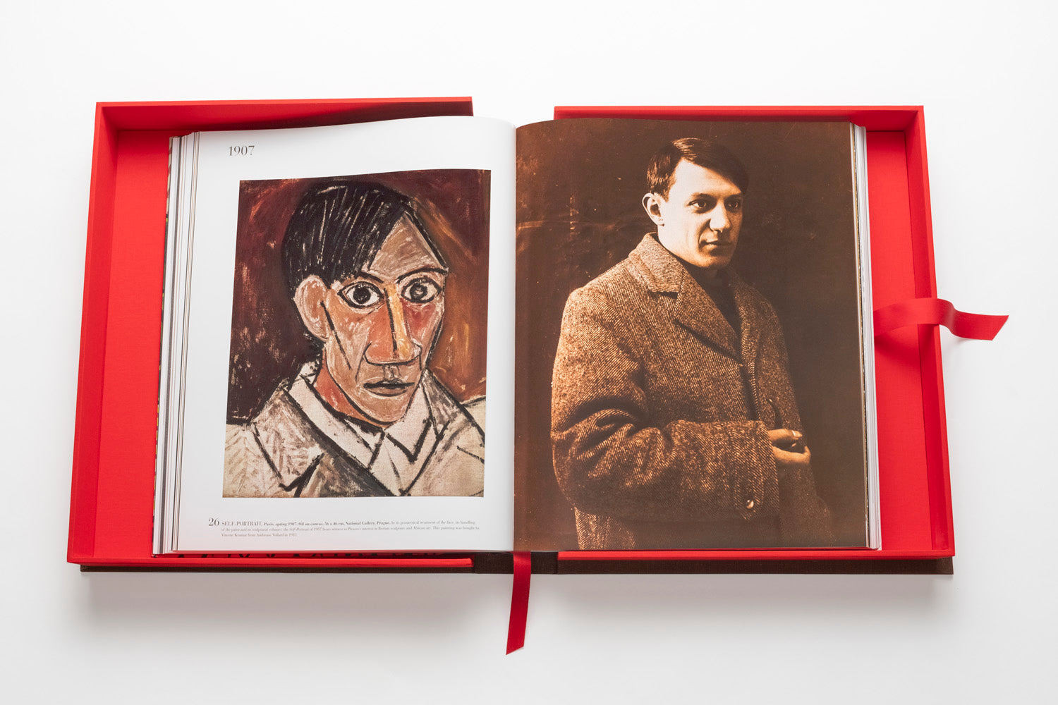 An open book with a red cover shows a painting of a person on the left page and a photograph of a man in a coat on the right page, reminiscent of The Impossible Collection: Picasso, celebrating influential artists of the twentieth century.