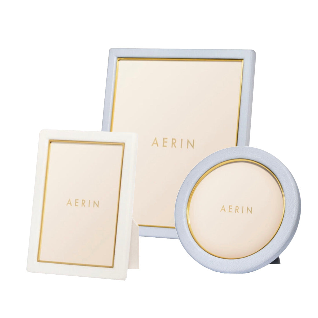 Three pieces from the AERIN Classic Piero Leather Frame Collection in different shapes and sizes, including rectangular and round, featuring gold detailing for an elegant display.