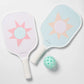 The SUNNYLiFE Pickleball Set in Rio Sun Multi features two pastel sunburst pickleball paddles and a mint green perforated ball, crafted with durable carbon fibre, displayed on a white surface.