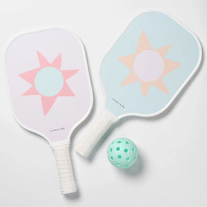 The SUNNYLiFE Pickleball Set in Rio Sun Multi features two pastel sunburst pickleball paddles and a mint green perforated ball, crafted with durable carbon fibre, displayed on a white surface.