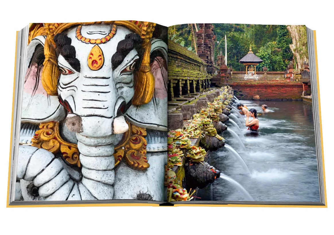 An open book, Bali Mystique, displays an image of a Ganesha statue on the left page and people bathing in a stone water fountain at a temple in Bali on the right page.