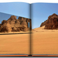 A photograph in an open book shows the arid desert terrain of AlUla, with rock formations and a mirrored building reflecting the landscape in this stunning UNESCO World Heritage Site in Saudi Arabia, known as AlUla Ever.