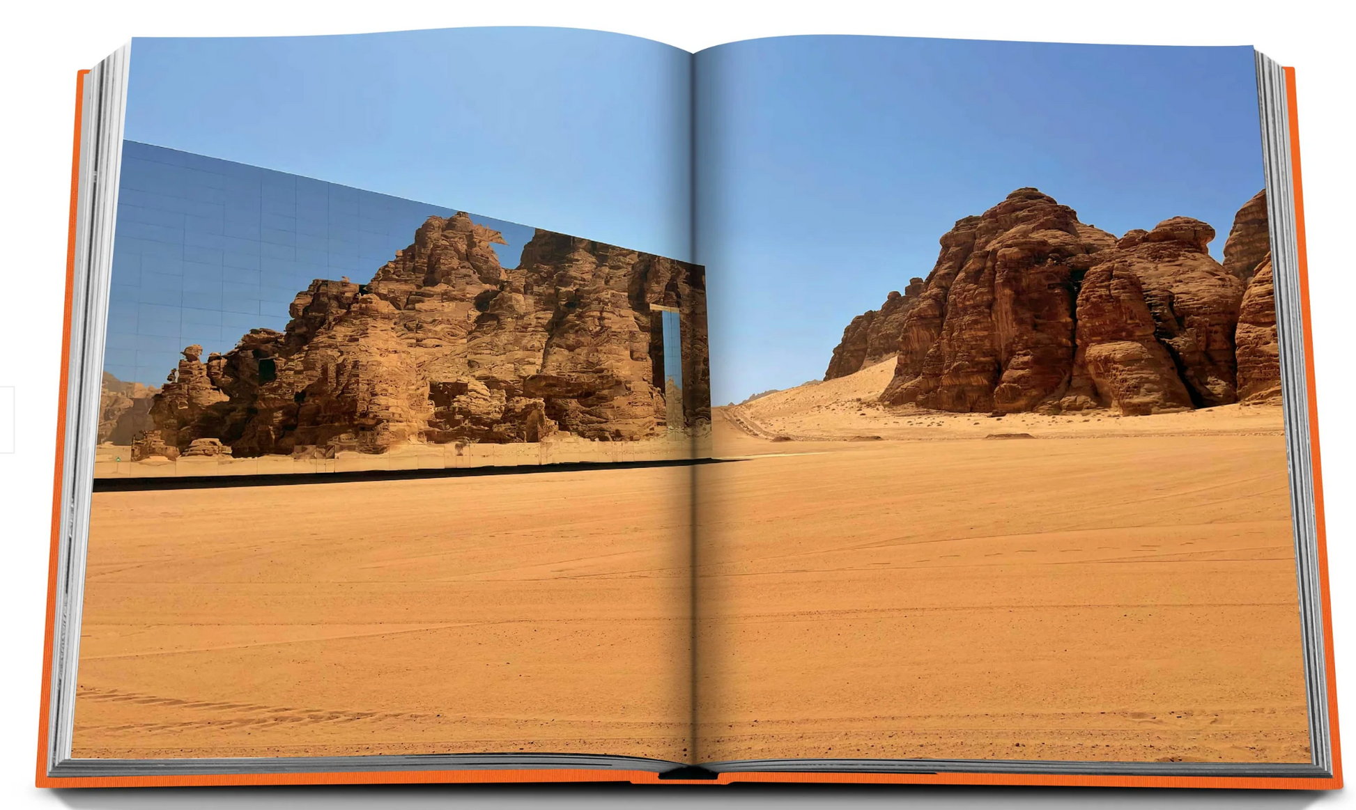 A photograph in an open book shows the arid desert terrain of AlUla, with rock formations and a mirrored building reflecting the landscape in this stunning UNESCO World Heritage Site in Saudi Arabia, known as AlUla Ever.