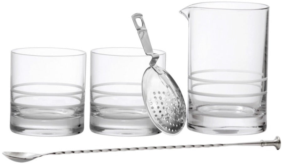 Introducing the Fortessa Crafthouse 5-Piece Mixing Set, featuring a set of clear glass tools including two tumblers, a mixing glass with a spout, a metal strainer, and a stirring spoon with a twisted handle. Designed in collaboration with Charles Joly, it's perfect for any home bar.