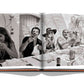 A black-and-white photograph in an open book shows a group of people at a sunlit outdoor table in St. Tropez, smiling and laughing. The table is set with plates, glasses, and a bottle, capturing the essence of St Tropez Soleil.