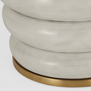 Close-up of the bottom part of a white, rounded ceramic object with a smooth finish, reminiscent of Kelly Wearstler's artistic touch. The Phoebe Extra Large Stacked Table Lamp, Antiqued White rests on a circular, gold-colored metallic base, seamlessly blending contemporary and vintage aesthetics.