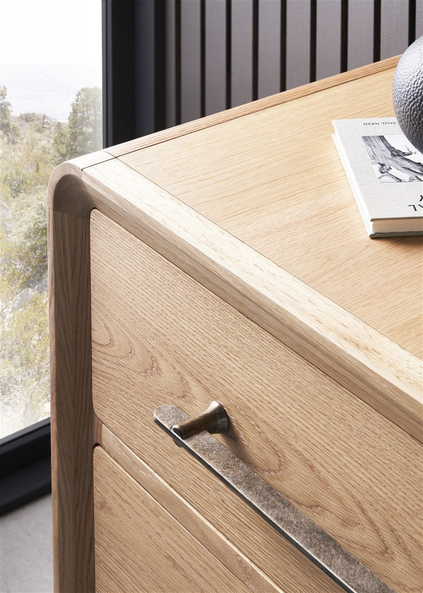 Close-up of the Form Dresser in light wood with spacious drawers and organic bronze pulls, topped with a book and decorative object, positioned near a window overlooking trees.