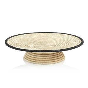 The Zodax Martigues Abaca Bowl Collection features a round handwoven basket with concentric circles, a beige design, a slightly raised base, and a black rim. This piece showcases native craftsmanship and intricate cultural details.