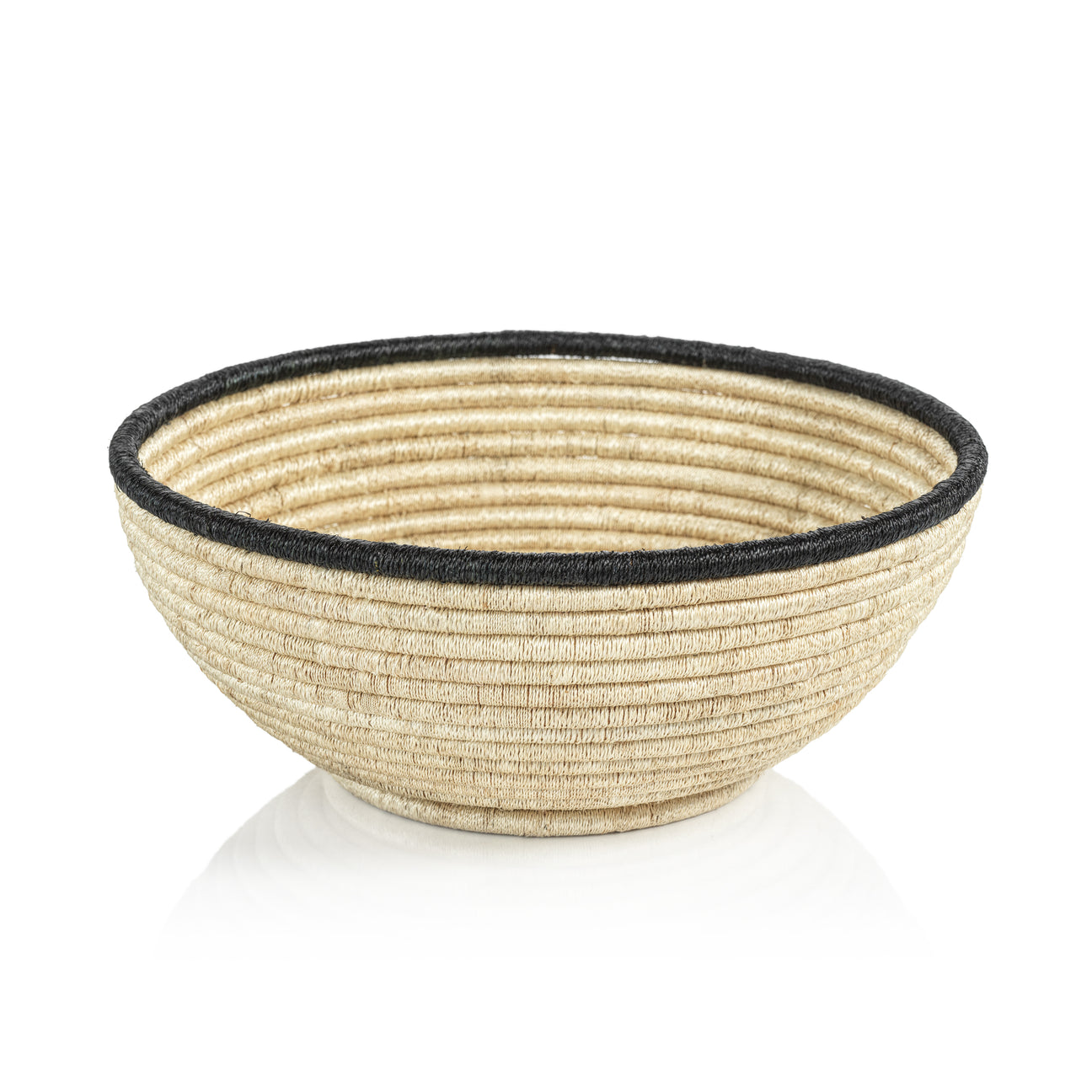 Displayed on a white reflective surface, the Zodax Martigues Abaca Bowl from our collection showcases native craftsmanship with its handwoven straw and black rim.